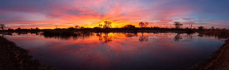 Fiery sunrise, trees in silhouette and reflections in water in the Australian Outback 