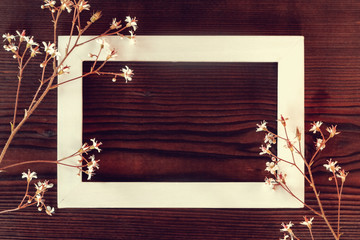 White wooden frame on a dark wooden background with small flowers - a template for a greeting card or invitation