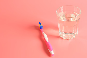 toothbrush and a glass of water on a pink background