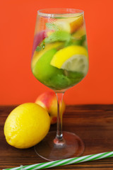 Summer refreshing long drink with lemon, nectarine and lime. Glass of alcoholic gin tonic cocktail with fresh fruits and mint on orange background.