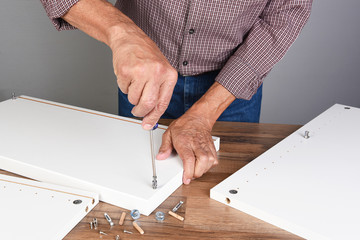 Fototapeta na wymiar A man assembling a DIY piece of furniture. Person is using a screwdriver inserting a piece of hardware