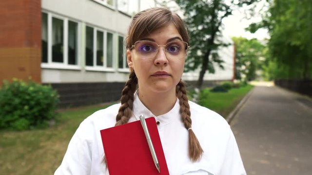 Portrait of the beautiful woman in glasses and with long fair hair looking straight in the camera seriously. She is a strict teacher or a smart student or a qualified doctor, schoolgirl, graduate stud