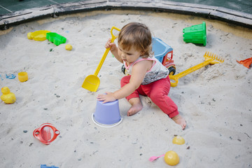 Fototapeta premium Baby girl in sandbox playing with toys