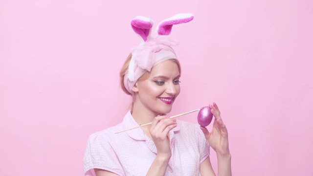 Funny Easter bunny painting egg. Sexy blonde pinup girl with bunny ears. Woman in bunny ears. Sexy pin up female model dressed in costume Easter bunny. Pin up style.