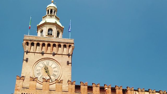 Close up of Accursi tower is also known as the Clock Tower of Palazzo d'Accursio or Comunale, Piazza Maggiore, Bologne in Italy in the blue sky. SLOW MOTION
