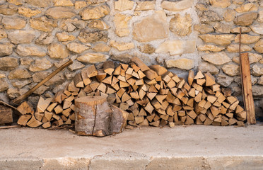 Chopped wood and axe stacked against the stone wall of a rustic farmhouse