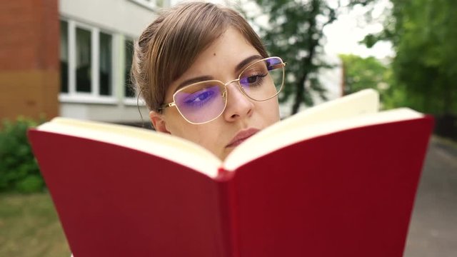 Serious  young girl in glasses reading book near school, university, motivated student with big dreams studying abroad, creative happy manager starts successful career