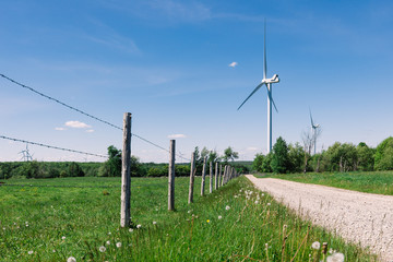 Fototapeta na wymiar Wind Turbines in a Green Field Near an Old Farm Fence