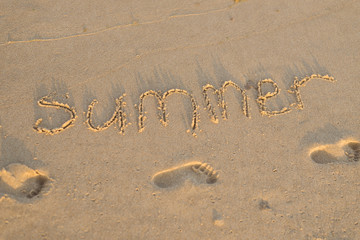The word summer on the sand and prints of children's feet on the beach, ocean.