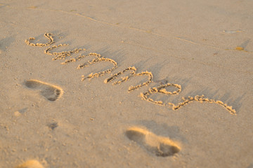 The word summer on the sand and prints of children's feet on the beach, ocean.