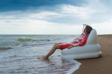 A contented, joyful woman rests on the beach in a raincoat during rain.