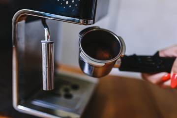 Barista holds a portafilter with coffee to make espresso. A woman's hand holds a metal portafilter with ground coffee on the background of the coffee machine. Concept of making coffee. Toned picture