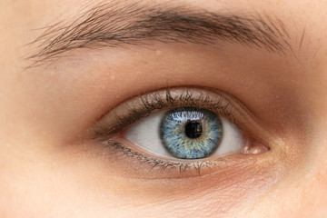 A closeup view on the blue iris and eye of a thirty something Caucasian lady. Pretty girl with minimal makeup looks into a macro lens. Detailed vision and beauty concepts.