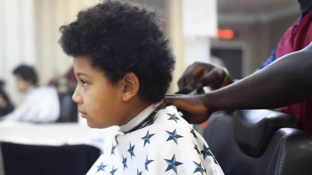 Boy in the african barbershop. Cute mixed boy makes a haircut in the African salon. Hair style. Haircut by machine for children. School boy hair style. Haircut by scissor