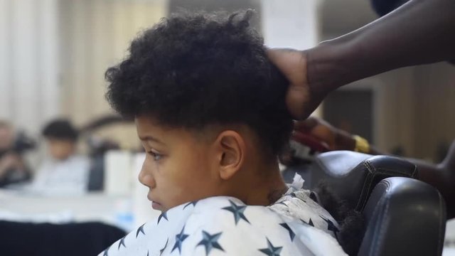 Boy in the african barbershop. Cute mixed boy makes a haircut in the African salon. Hair style. Haircut by machine for children. School boy hair style. Haircut by scissor