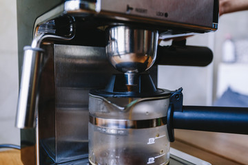 Ready hot coffee flows through the portafilter into a glass mug. Coffee flowing in beaker mug with portafilter on coffee machine on wooden table in cafe background. Toned photo
