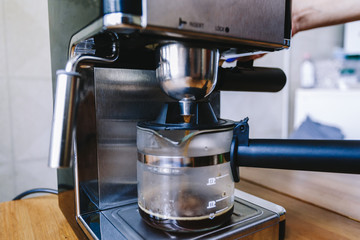 Ready hot coffee flows through the portafilter into a glass mug. Coffee flowing in beaker mug with portafilter on coffee machine on wooden table in cafe background. Toned photo