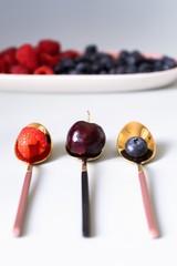 Summer berries blueberries, raspberries and cherries on the new elegant plates of pink, blue and gray colors. New luxury Golden cutlery view from above on a isolated white background. Top view.
