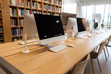 Wooden interior of the library with panoramic windows with a wooden table with computer monitors on...