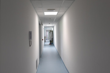 Lab jackets are seen blurred in the background of a long passageway inside a technology and research facility. Long white walls lead down a futuristic building.