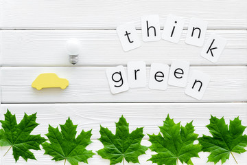 Think green text with car toy, lamp, green maple leaves on white wooden background top view
