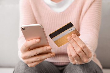 Young woman with credit card and mobile phone shopping online at home, closeup