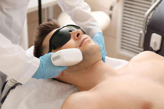 Handsome man undergoing procedure of laser hair removing in beauty salon
