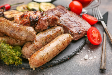 Slate plate with tasty grilled meat with sausages and vegetables on grey background