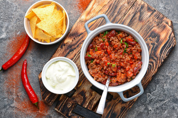 Pot with tasty chili con carne and sauce on grey background