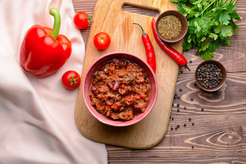 Bowl with tasty chili con carne on wooden background