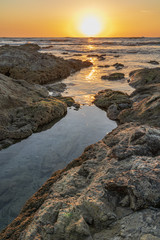 Sunset over the ocean horizon reflecting along the rocks