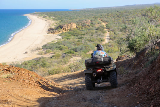 Two people riding an ATV down a dirt road along the coast in the Baja, Mexico. 