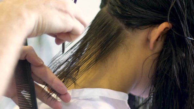 Professional hairstylist cuts model's hair with a razorblade upclose.