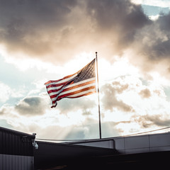 An American Flag illuminated by by rays of sunlight through a threatening sky