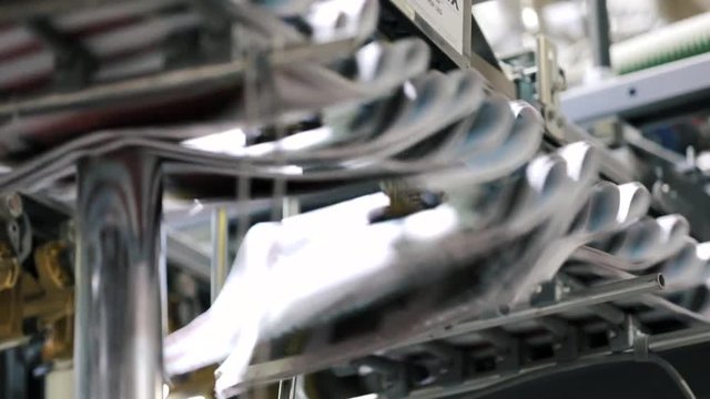 Newspapers move at high speed through the folding section of a rotary press inside a printing house. Bright metal guides and rollers carry the folded pages along a busy precise production line.