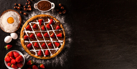 Obraz na płótnie Canvas brazilian sweet pizza with hazelnut cream and strawberry on black concrete background.