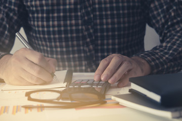 Business man Using calculator analyzing investment chart and writing note on the desk working at office. business concept.