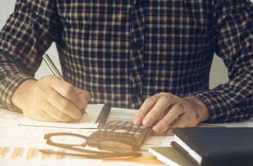 Business man Using calculator analyzing investment chart and writing note on the desk working at office. business concept.