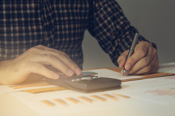 Business man Using calculator analyzing investment chart and writing note on the desk working at office. business concept.