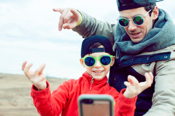 young father with his son having fun outside in spring field, happy family smiling, lifestyle people making selfie wearing sunglasses