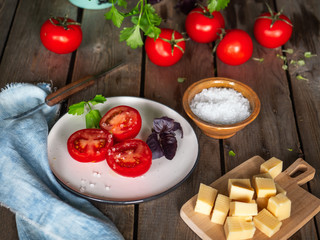 Rural sketch, a small lunch of chopped cheese and red tomato and a sprig of purple basil. Parsley greens in a ceramic mug, denim napkin on an old wooden board table shot from close range.