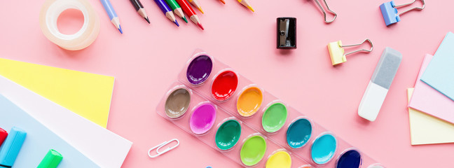 School supplies stationery, colour pencils, paints, paper on pink background, back to school concept with free copy space for text, modern elementary education. Kids desk, flat lay, top view, mockup.