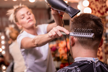 The master cuts the hair and beard of a man in a barbershop, a hairdresser does a haircut for a young man. Beauty concept, self care.