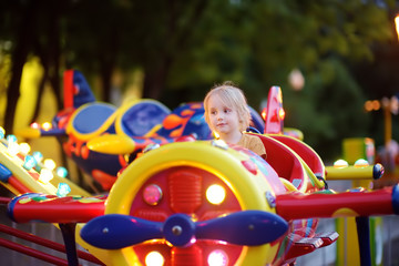 Little boy having fun on attraction in public park. Child riding on a merry go round at summer...