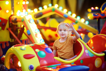 Little boy having fun on attraction in public park. Child riding on a merry go round at summer...