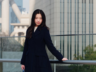 Portrait of young Asian woman with black long hair, smiling and happy with modern city background.
