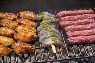 Mixed assortment of marinated meat, chicken, and prawns grilling on hot coals on a BBQ