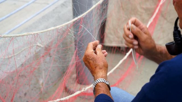 Old fisherman reparing fishing net during the day.