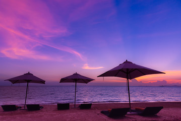 The beautiful beach umbrellas and chairs on sand beach with twilight and blue sky background in evening time to relax.