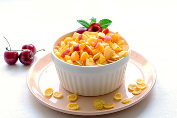 Healthy breakfast with cornflakes and pieces of fruit, cherries on a white background